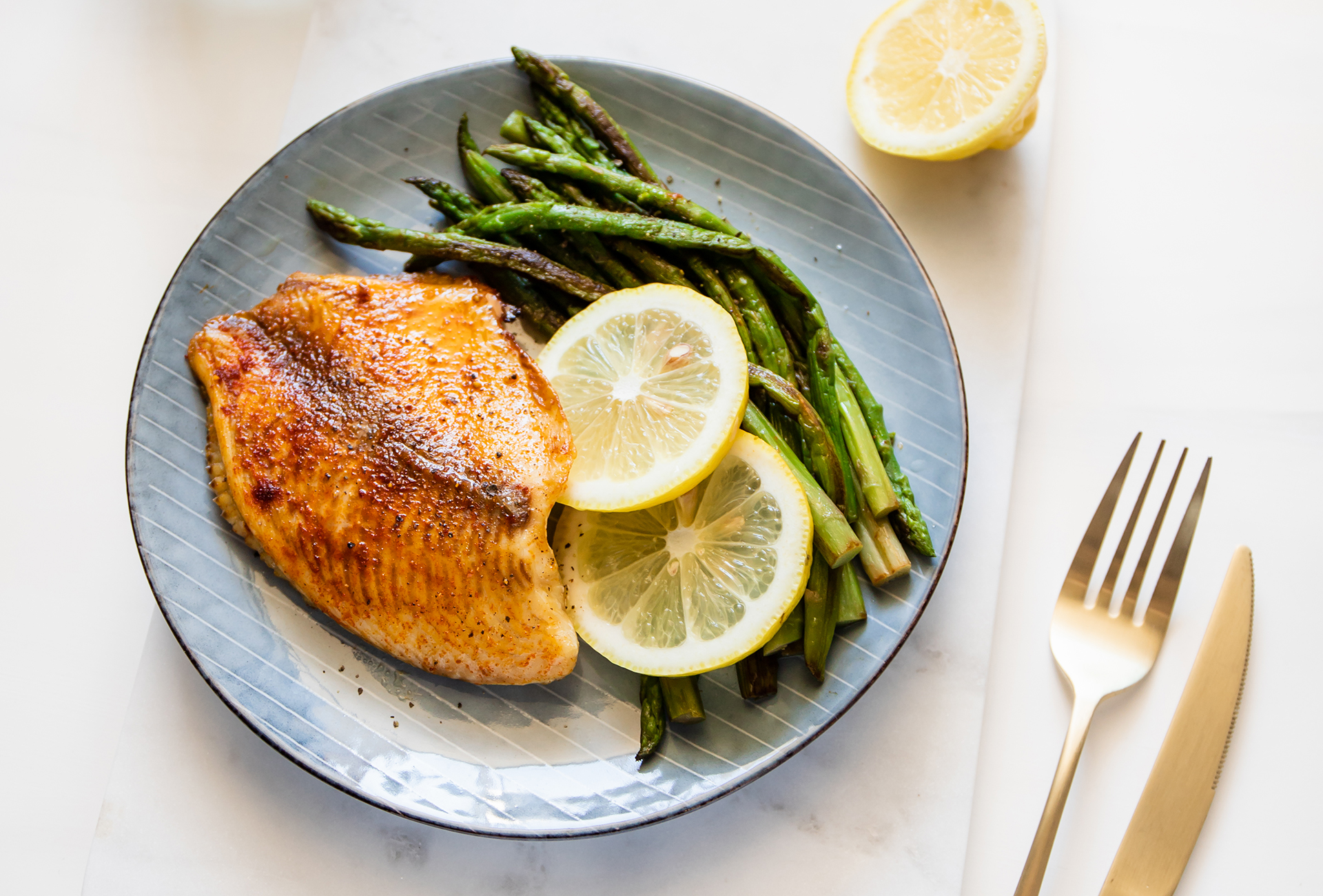 Roasted tilapia fish with asparagus on a ceramic plate. Healthy mediterranean diet lunch or dinner. Top view, flat lay.